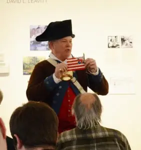 At the Putnam History Museum annual meeting, Col. Jim Johnson, in the guise of a Continental Army officer, displays an early Revolutionary War flag, complete with a version of the British Union Jack, that indicated colonists' mixed loyalties.