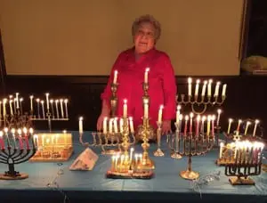 Rhoda Needleman with some of the many menorahs brought to the service. (Photo provided)