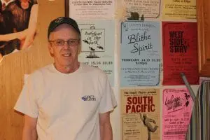 Bill Peckham, who has been involved with County Players for decades, pictured in a dressing room plastered with flyers from previous shows. (Photo by A. Rooney) 