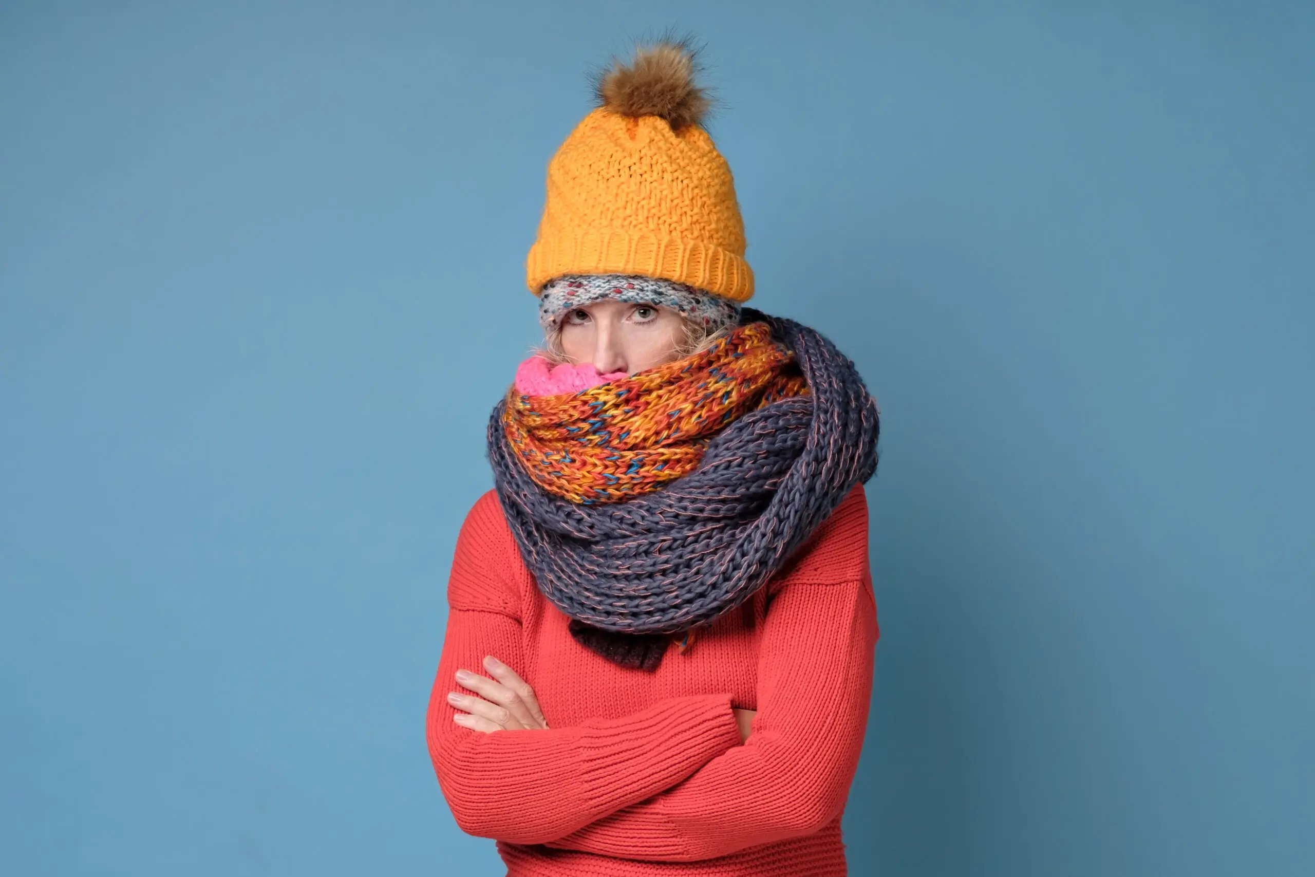 Funny senior caucasian woman wearing winter clothes being cold and frozen on blue studio wall