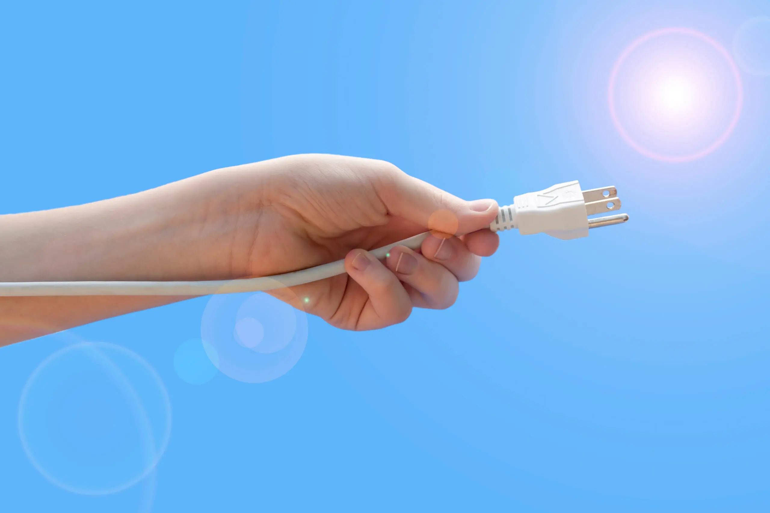 Youth hand holding electric plug on sky with sun flare