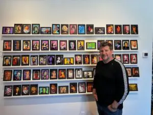 Coulter Young poses with reproductions of his portraits of musicians and other famous faces. Photo by M. Ferris