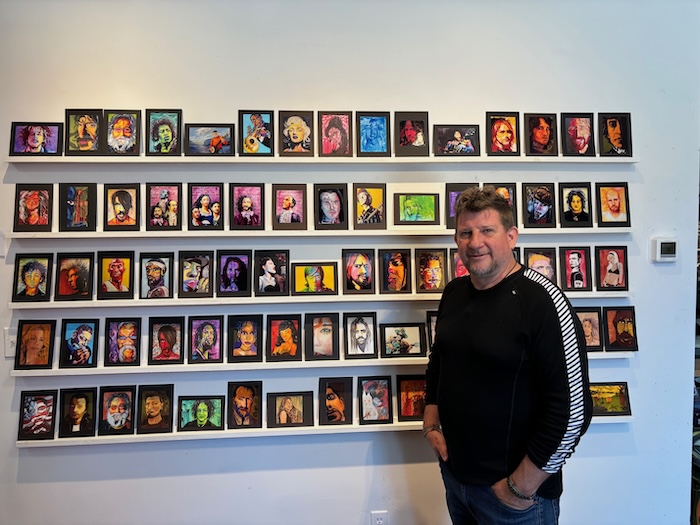 Coulter Young poses with reproductions of his portraits of musicians and other famous faces. Photo by M. Ferris