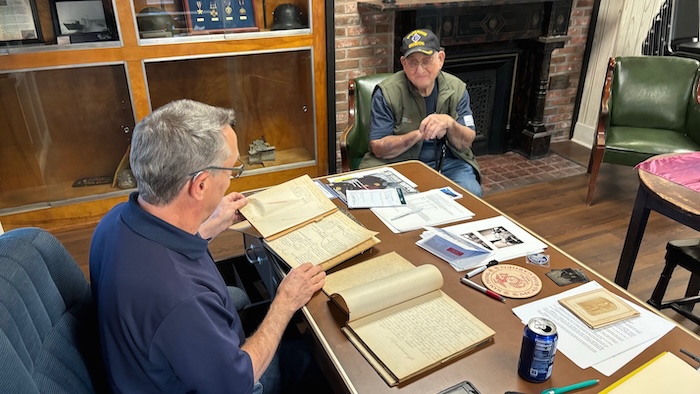 Harold Delamater (left), commander of the VFW post, and Paul Blose, commander of the American Legion post, look over the 1880s minutes of the Grand Army of the Republic. Photo by M. Ferris