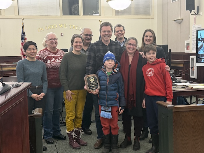 The City Council recognized Aymar-Blair at his last meeting on Dec. 16. From left: Paloma Wake, Pam Wetherbee, Molly Rhodes, Mayor Lee Kyriacou, Aymar-Blair, his son Henry (in blue), Jeff Domanski, Aymar-Blair’s wife Monika, Amber Grant and his son Leo (in red). Photo provided