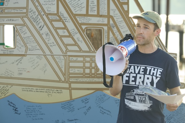 Carson Carter, an organizer from Newburgh, speaks at a rally on Tuesday calling for the return of the Beacon-Newburgh ferry. In the background is a cutout signed by supporters. Photo by Ross Corsair